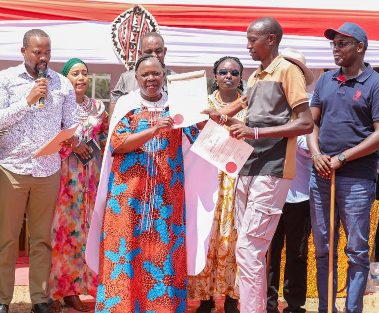 Cabinet Secretary for Lands, Public Works, Housing and Urban Development Alice Wahome presents a title deed to a beneficiary during the issuance of 60 community land and public utility title deeds in Samburu East